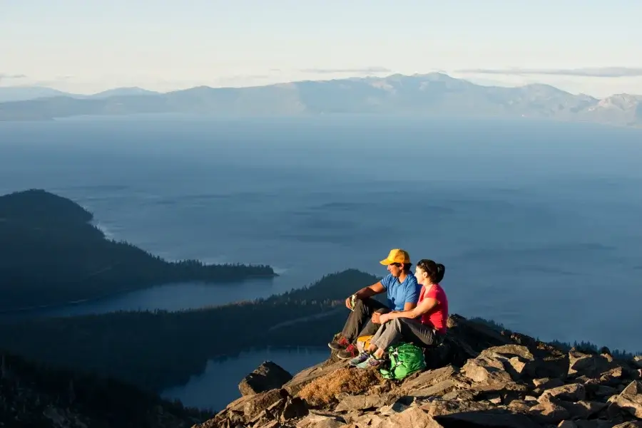 Two people sitting on the top of Mount Tallac overlooking Lake Tahoe, Emerald Bay, and Cascade Lake